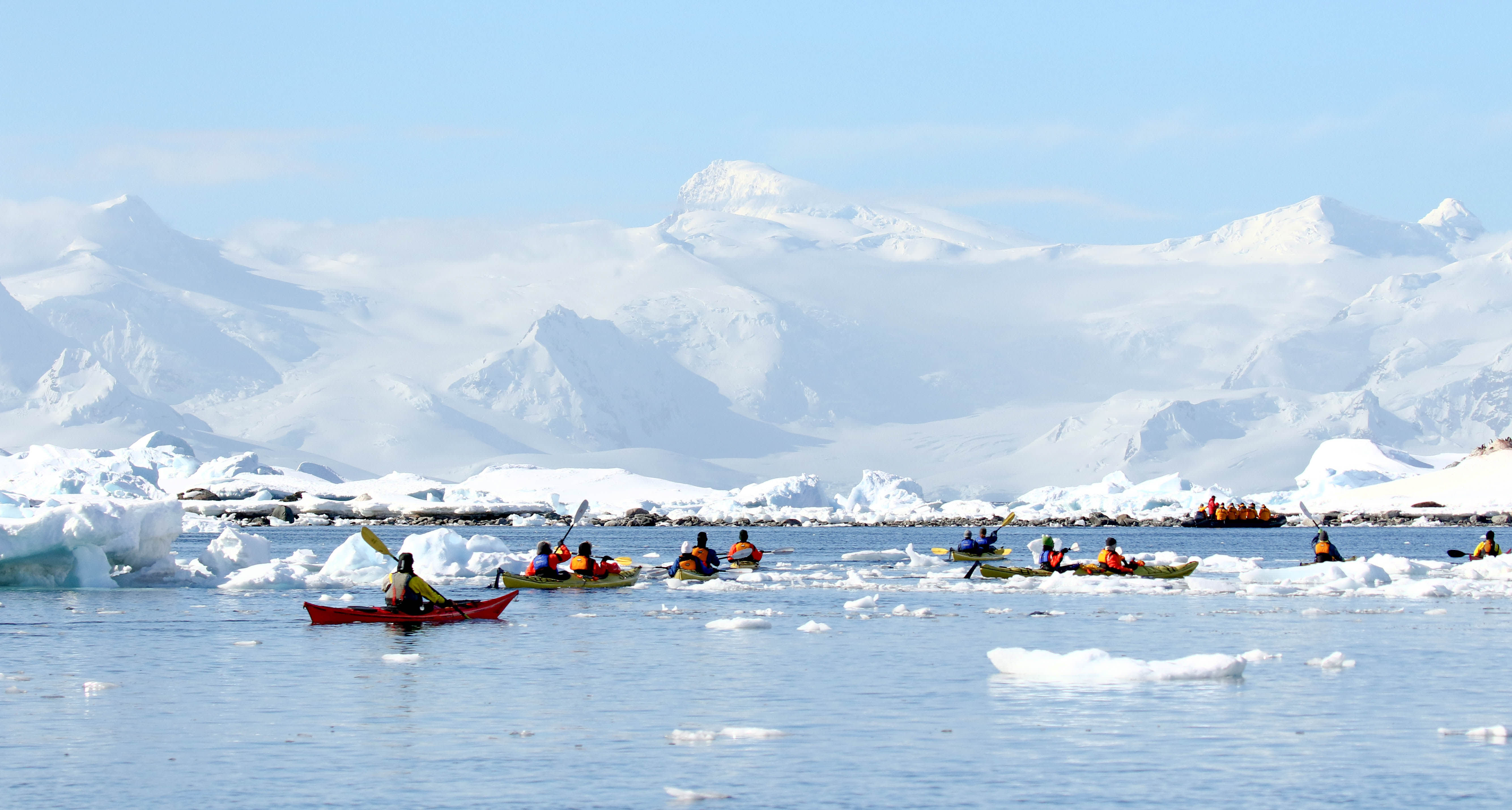 Guests kayaking through frigid waters in Antarctica. Two guides accompany the main group.